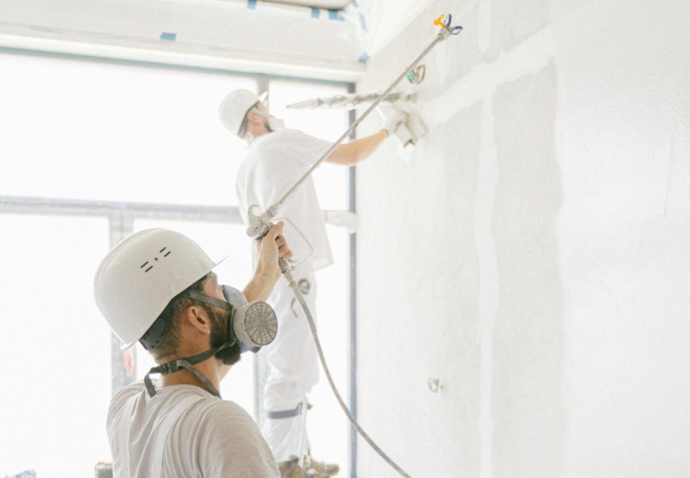 Two professional painters working indoors on wall renovation and painting project.